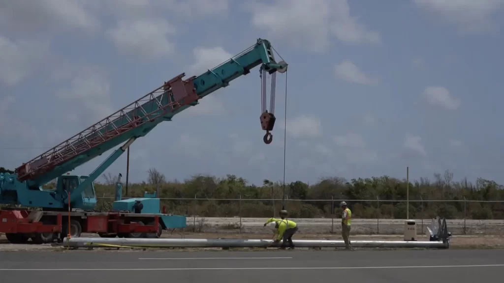 Crew rigging a 15.2 m galvanized steel apron lighting pole to a mobile crane before lifting at Burton–Nibbs International Airport