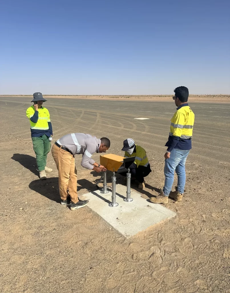 Aviation Renewables technicians in hi-vis adjusting a yellow Solar Series LED PAPI unit on its mounting legs