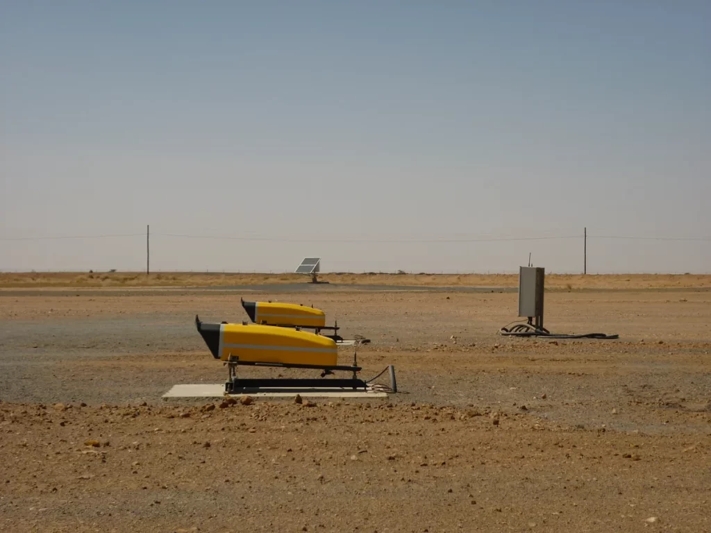 Two weathered yellow legacy PAPI units on a concrete pad, with the site's solar power system and control cabinet behind