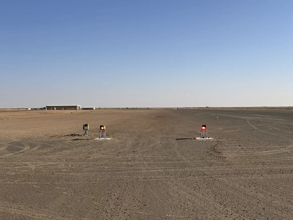 Solar Series LED PAPI units showing red lights on either side of a gravel mine airstrip, with a hangar on the horizon